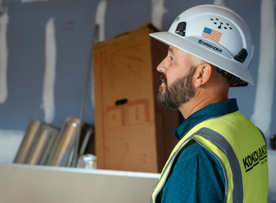 Bearded man in safety vest and hard hat indoors.
