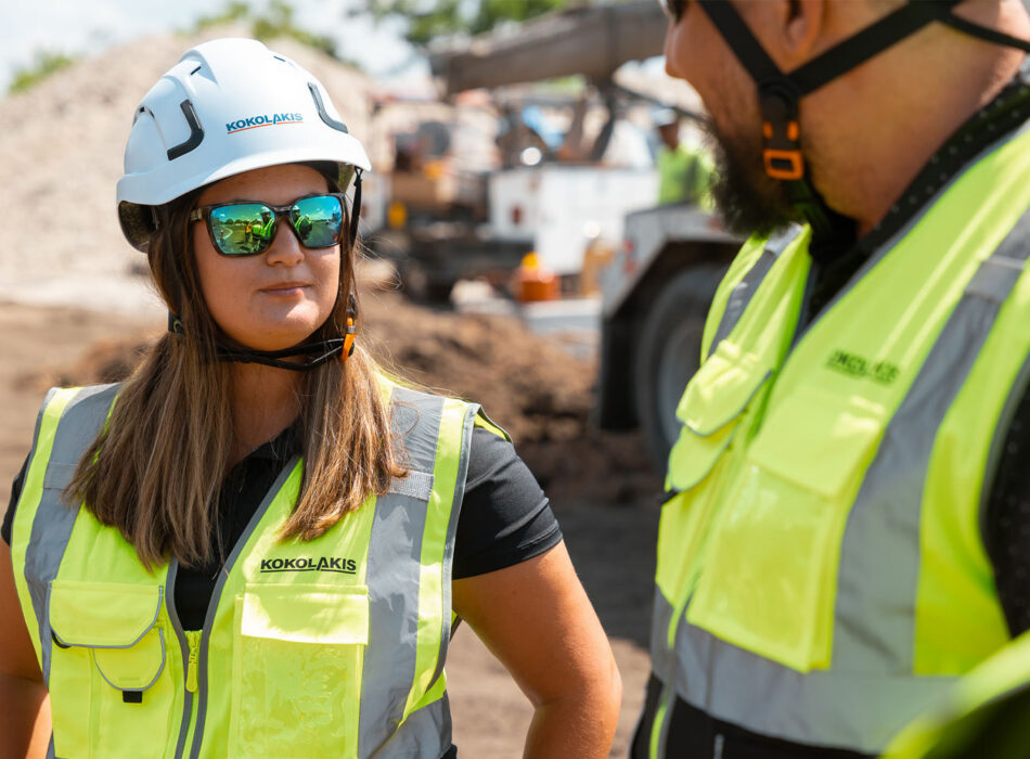 Two workers in vests talk at a construction site.