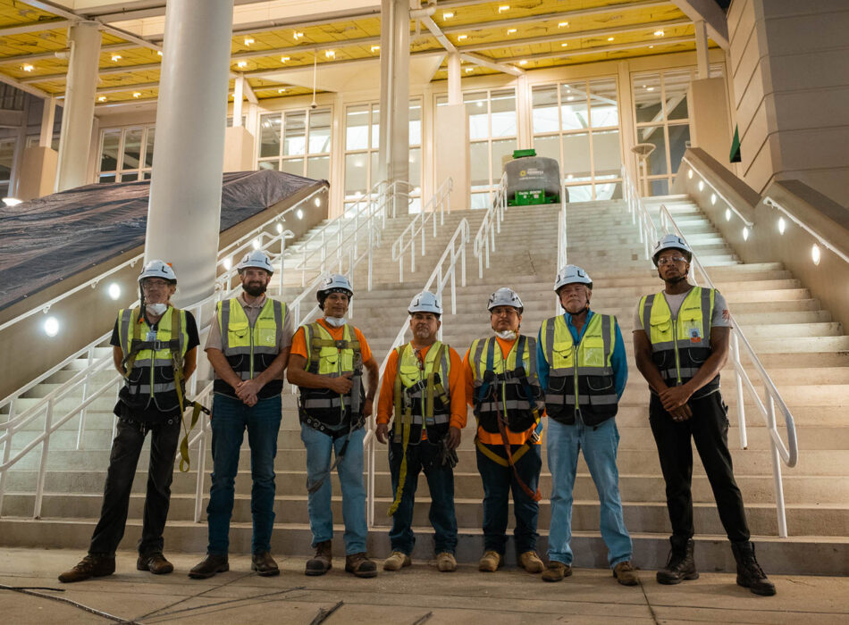 Seven workers in vests and helmets stand by building steps.