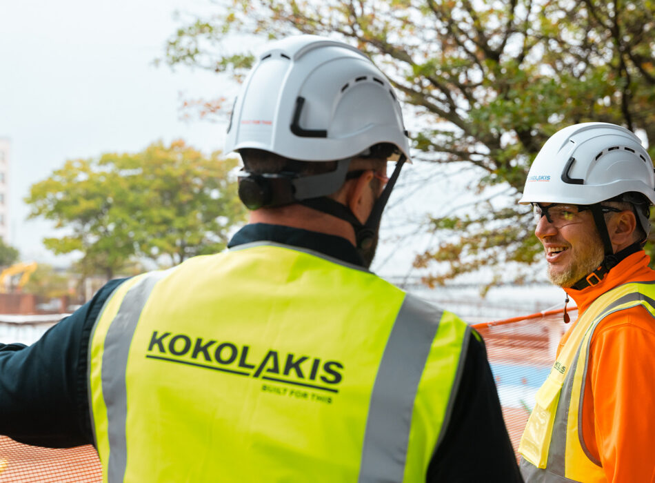 Two workers in safety gear talk at outdoor worksite.