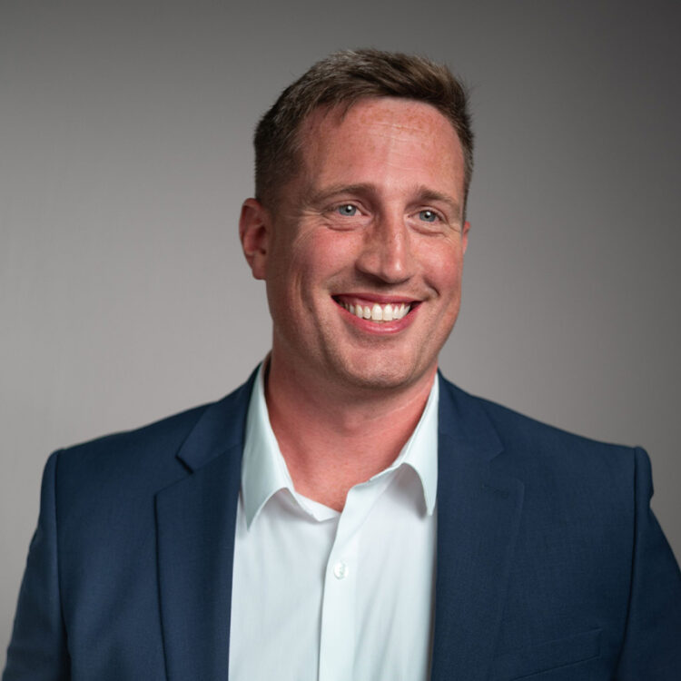 Man in blue suit smiling against gray background.