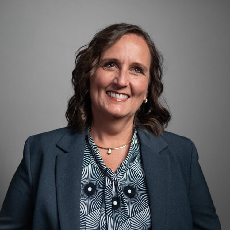 Smiling woman in blue blazer against gray background.