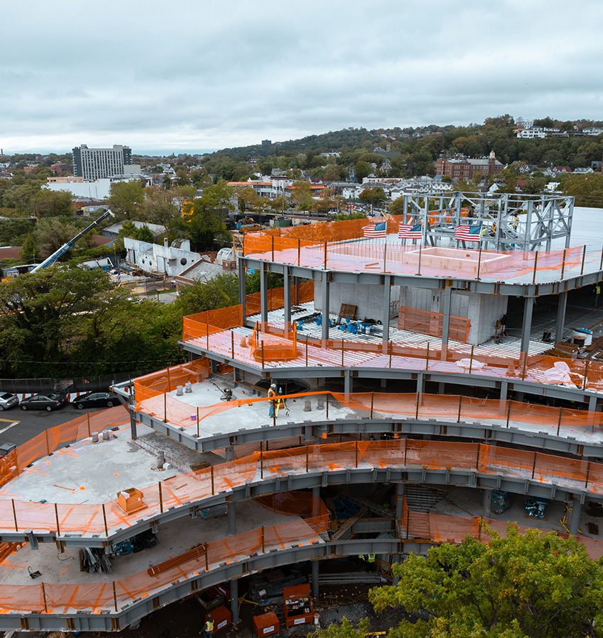 Building under construction with orange barriers and worker, cloudy day.