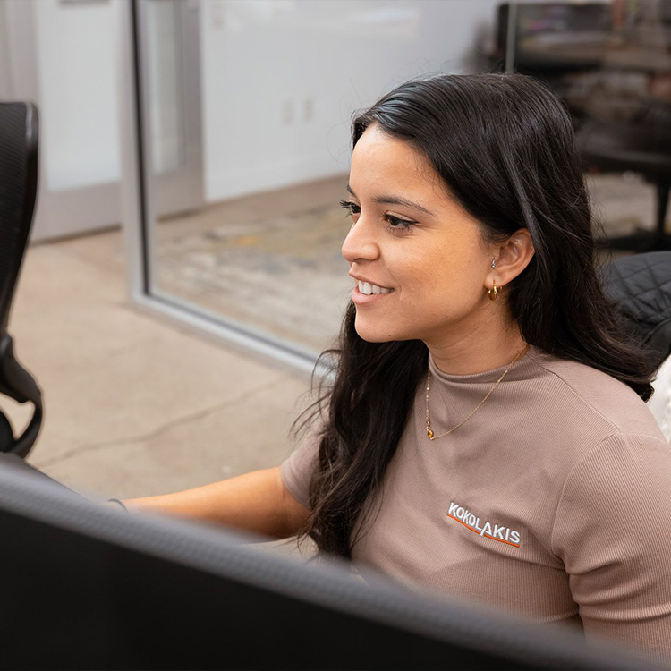 Smiling woman at desk in KOKOLAKIS shirt.