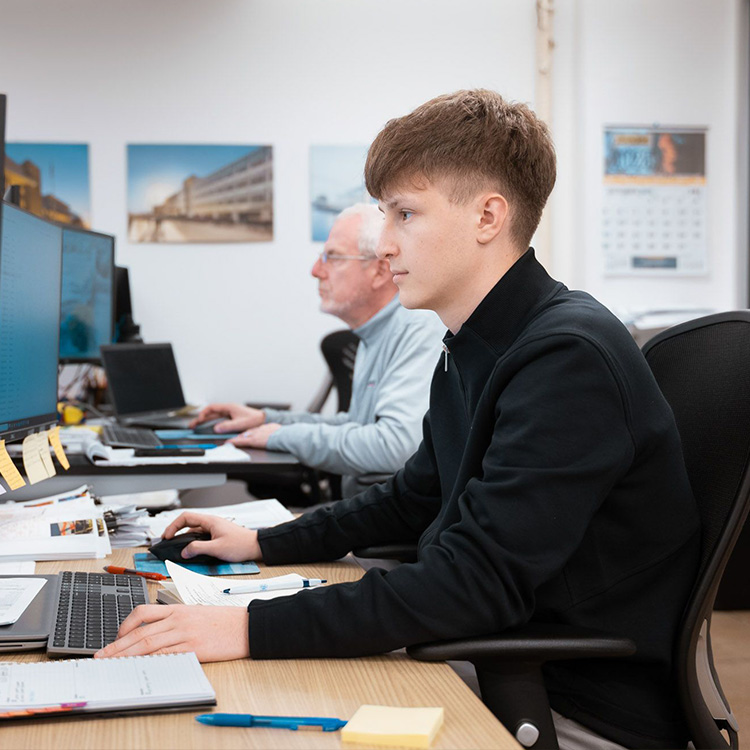 Two men work at desks with computers in office.