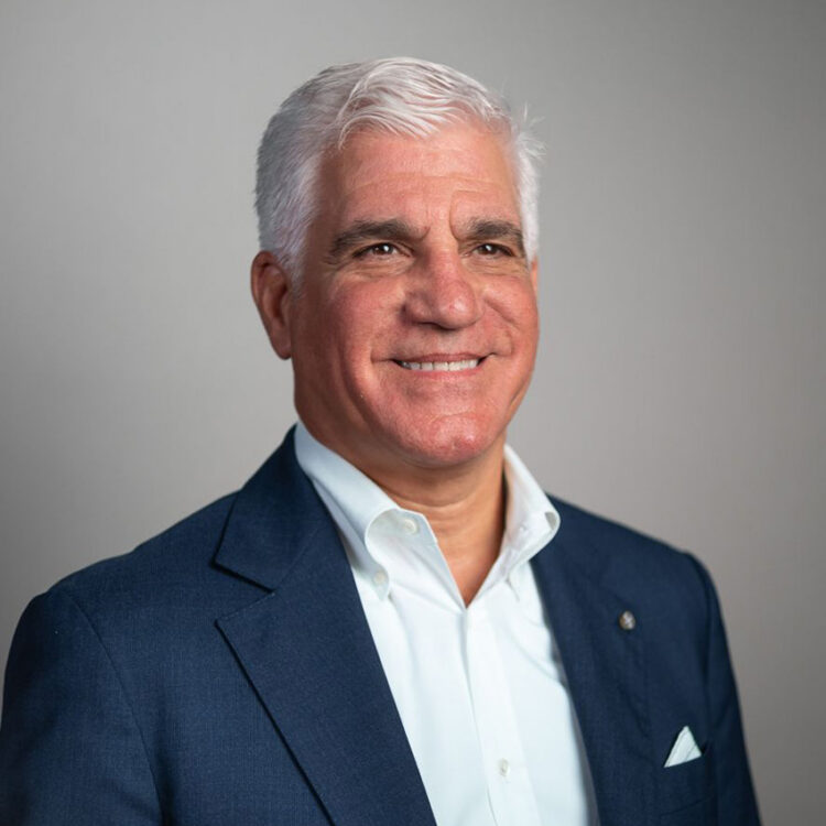 Smiling middle-aged man in navy suit, white hair.
