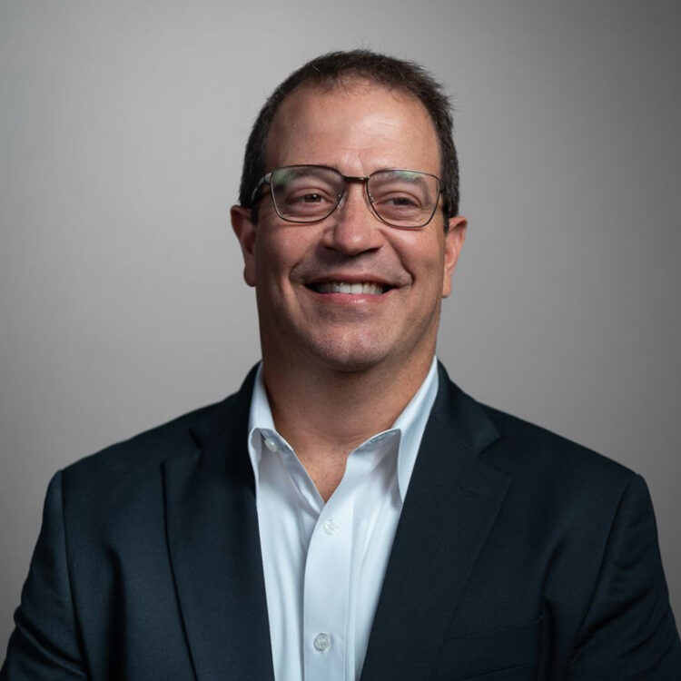 Smiling man in glasses, suit, and white shirt.
