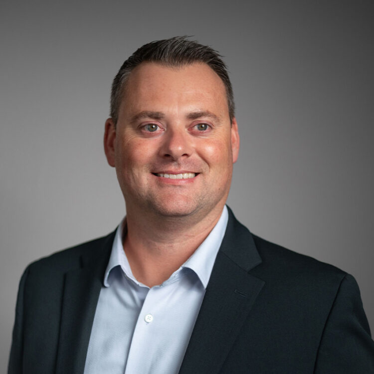 Smiling man in suit jacket, light shirt, gray background.