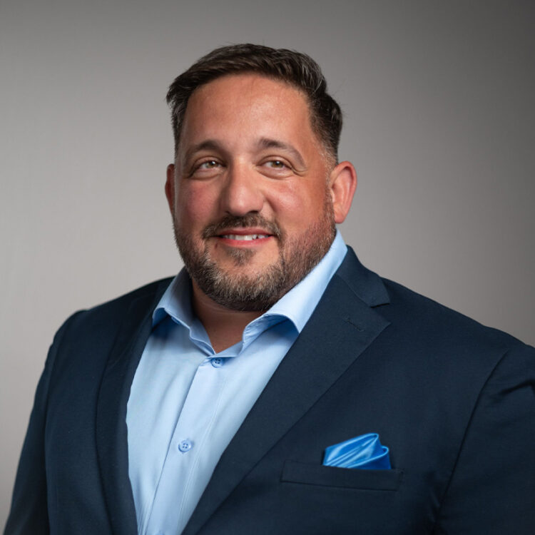 Smiling man in blue suit against light background.