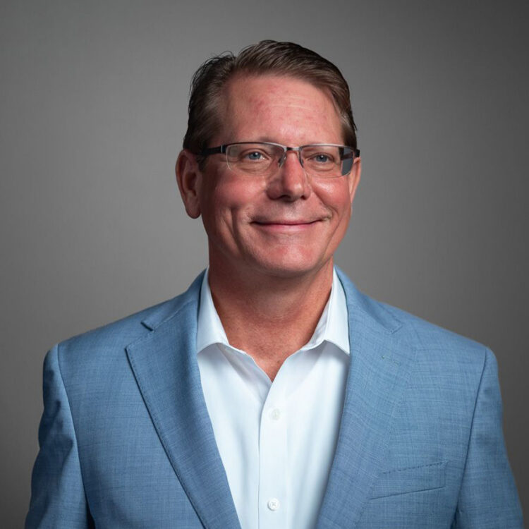 Man in glasses and blue suit jacket, slight smile.