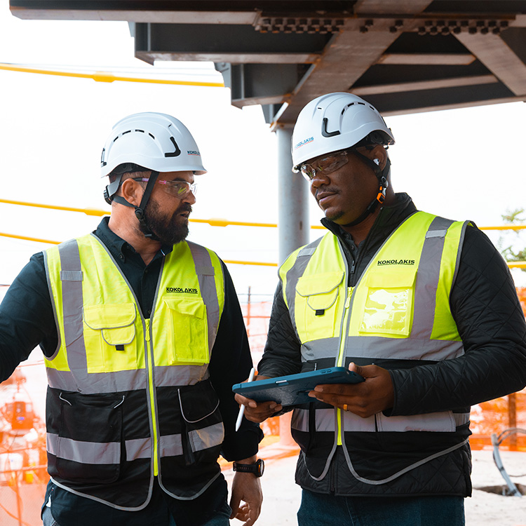 Two construction workers in vests and helmets discuss onsite.