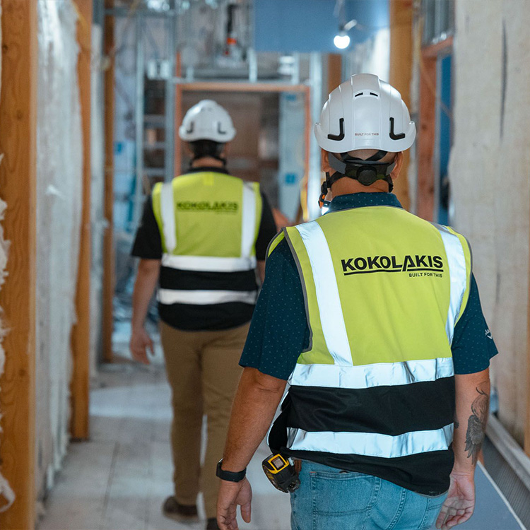 Construction workers in vests walk inside unfinished building.