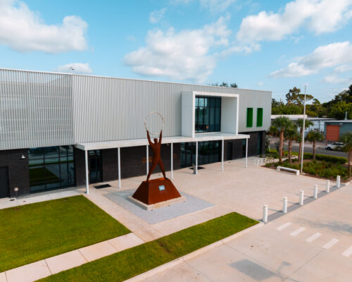 Modern building, lawn, and sculpture of figure with circle.