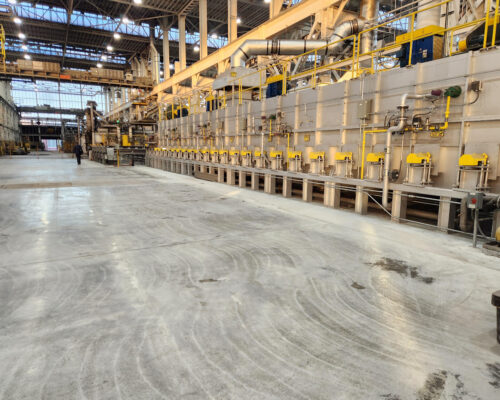 Factory interior with yellow machines, high ceilings, two people.
