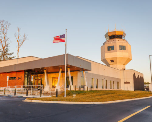 Airport control tower, office building, and American flag in daylight.