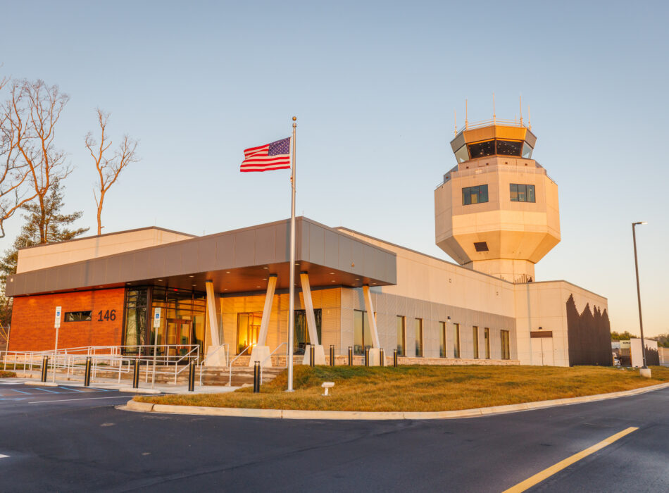Airport control tower, office building, and American flag in daylight.