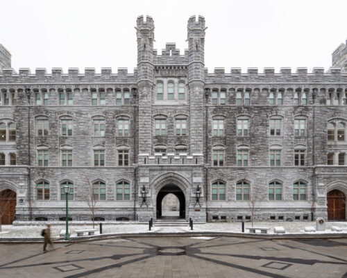 Stone building with towers, snowy ground, person walking by.