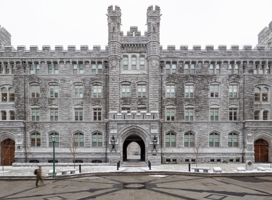 Stone building with towers, snowy ground, person walking by.