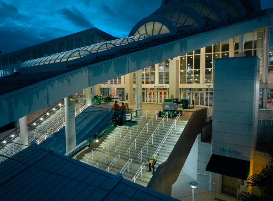 Workers use machinery on a lit outdoor staircase at night.