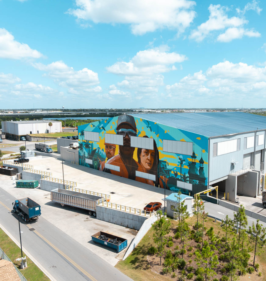 Warehouse with people mural, trucks, containers, blue sky.
