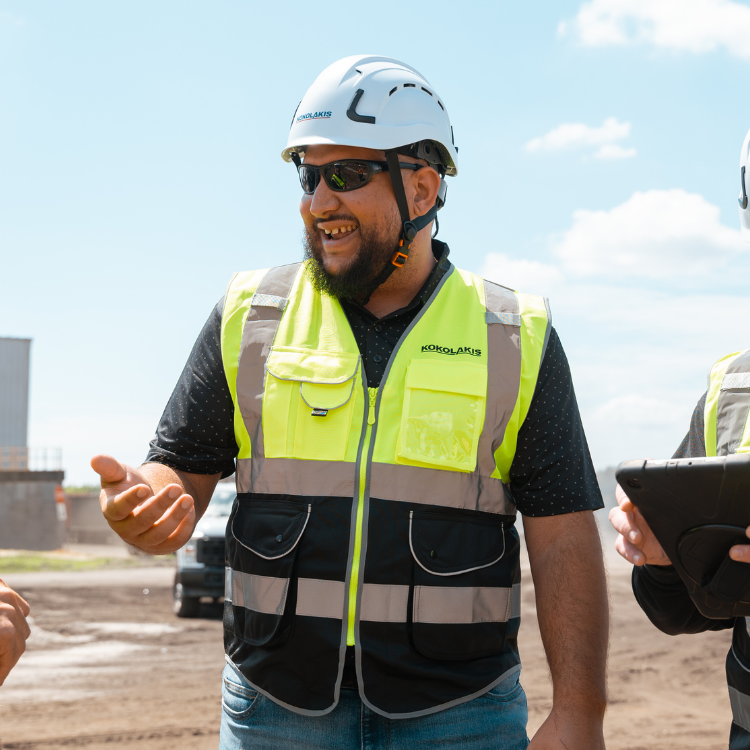 Smiling construction worker gestures outside in safety gear.