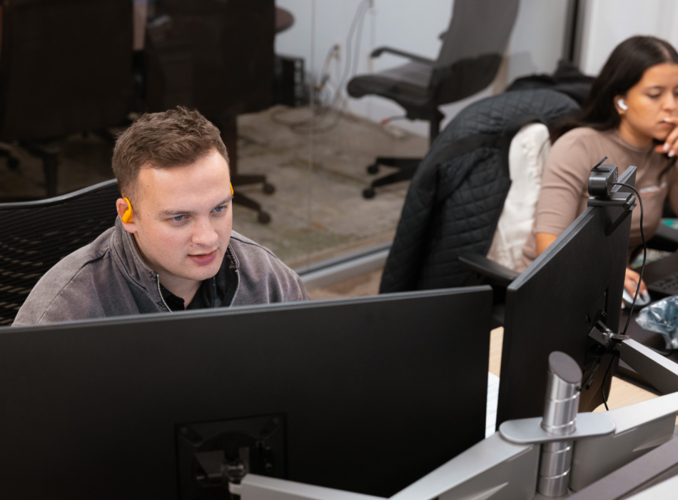 Two people work at desks with computers in an office.