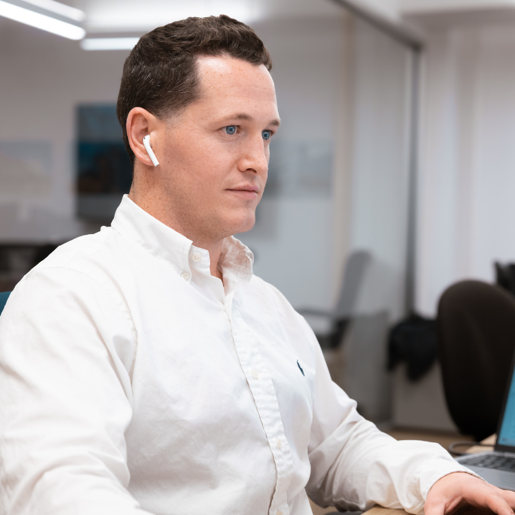 Man in white shirt at desk with earbuds and computer.