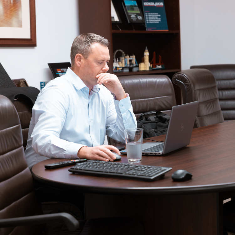 Man in white shirt works on laptop at conference table.