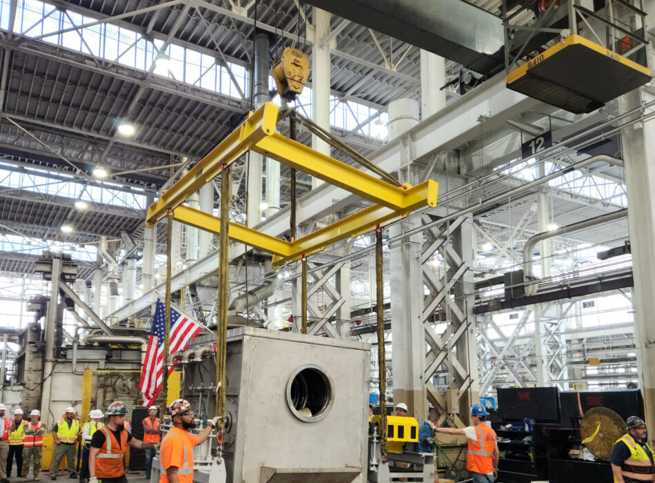 Crane lifts metal container; workers watch.