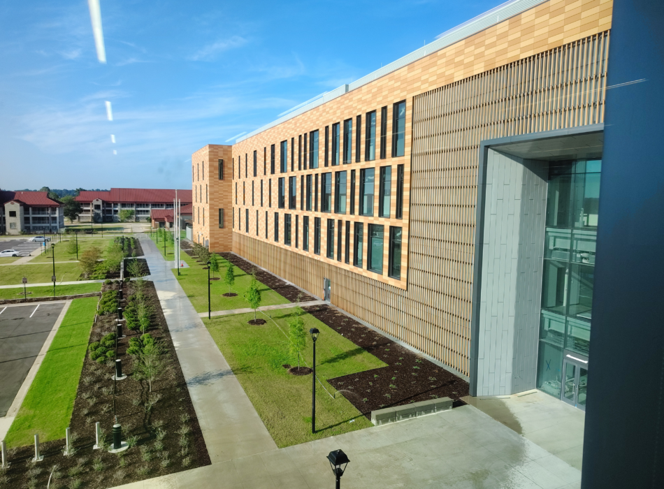 Modern brick and glass building with lawns under blue sky.