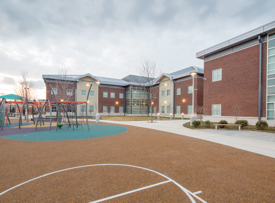 Brick school behind playground with climbing frames and court.