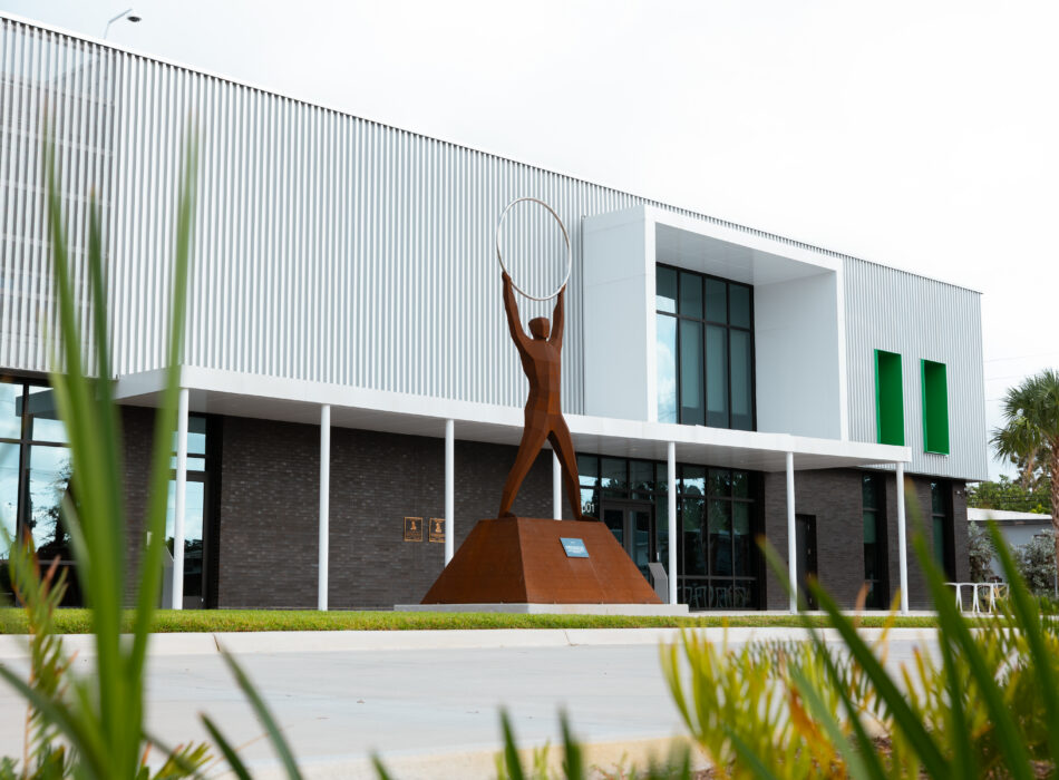 Modern building, green accents, metal statue with ring, palm landscaping.