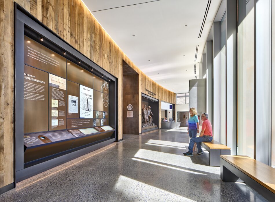 Two people sit on a bench in a museum hallway.