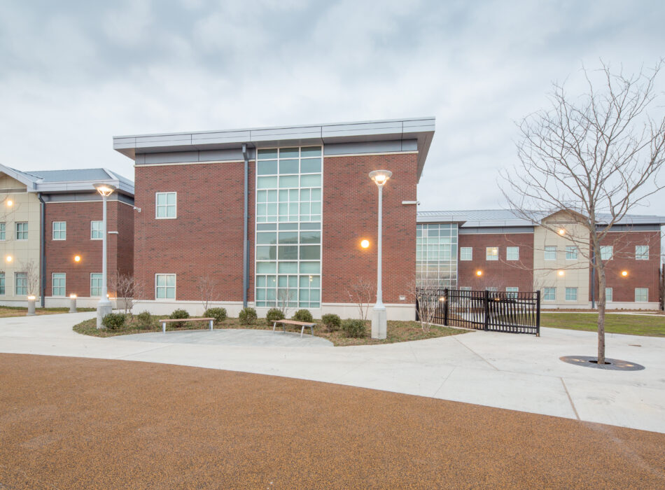Modern brick and glass building with exterior lights, leafless trees.