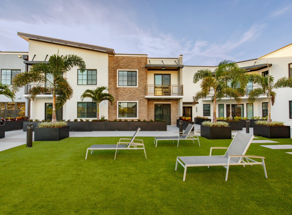 Apartment building, balconies, palm trees, lounge chairs on lawn.