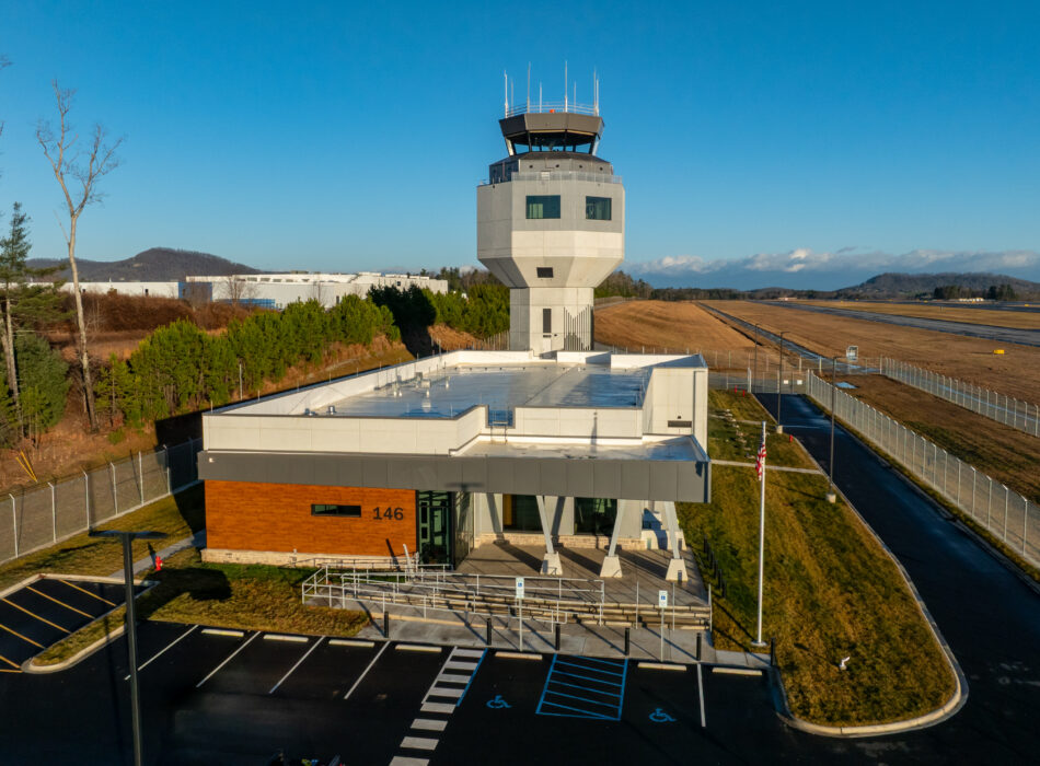 Aerial view of airport tower, building, runway, and trees.