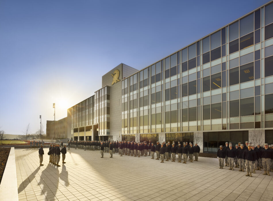 Uniformed group stands in formation outside modern glass building.