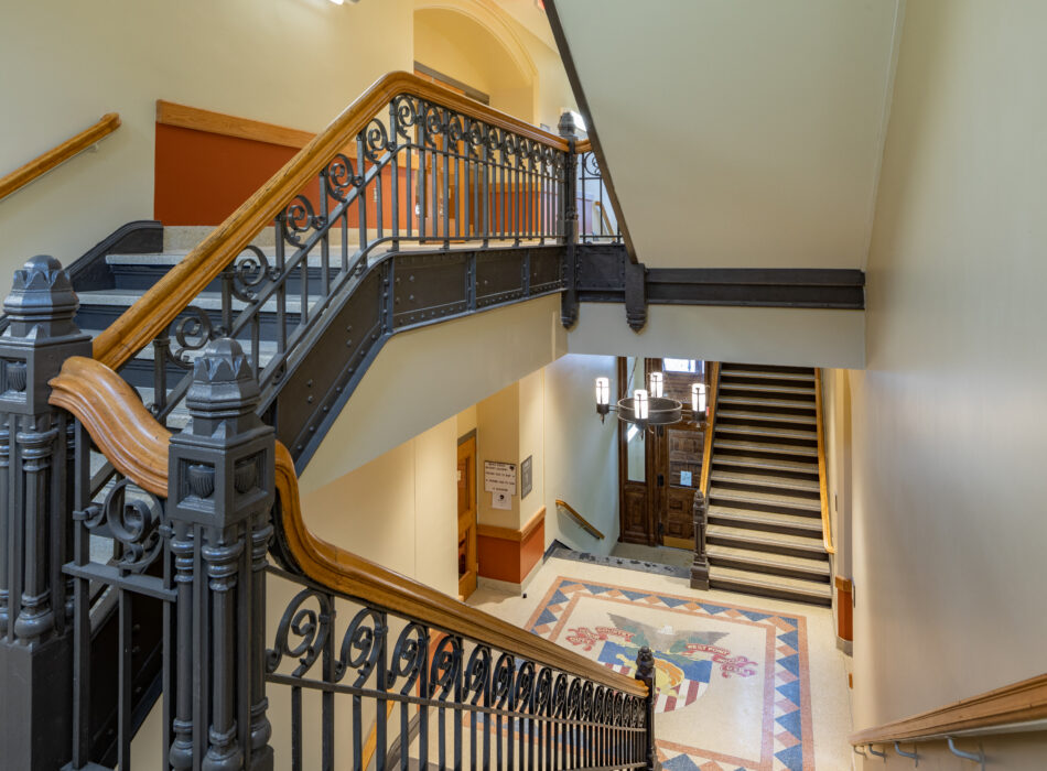 Staircase with metal railings, mosaic landing, yellow walls.