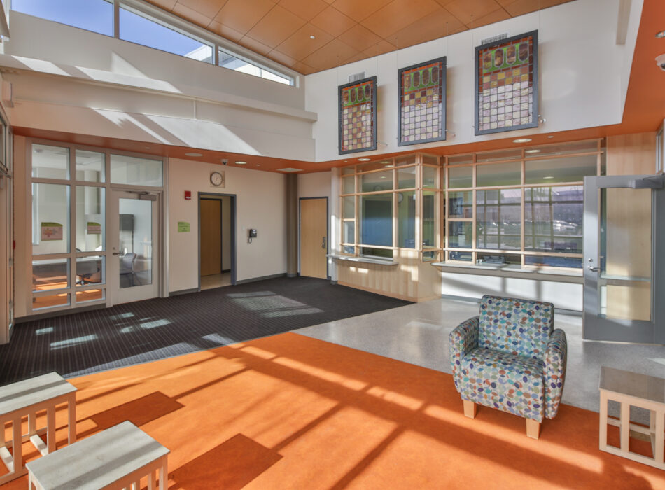 Bright lobby with orange floor, armchair, benches, windows.