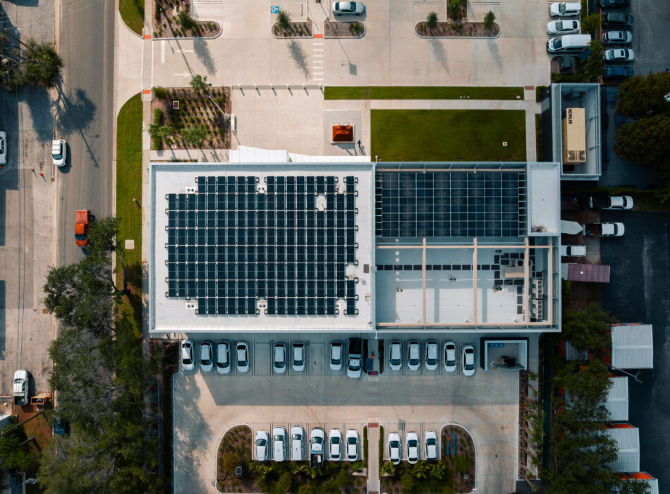 Aerial view: building with rooftop solar panels, parking lot.