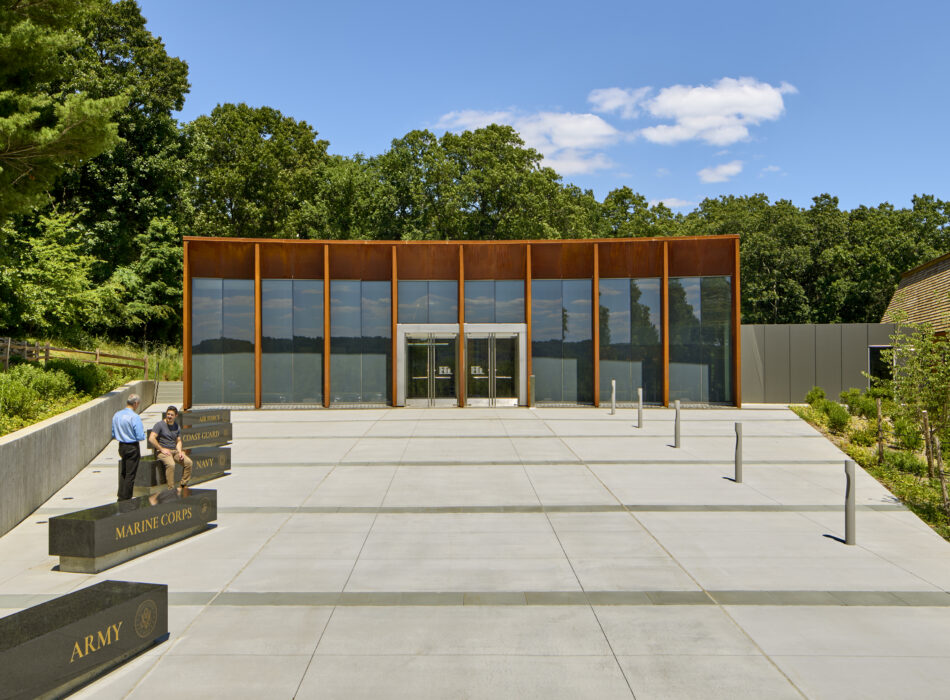 Modern glass building, trees, benches labeled Marine Corps, Army, Navy.