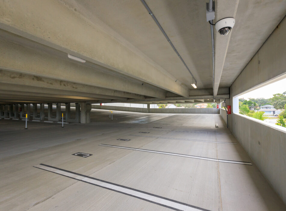 Empty garage, sunlight, parking spaces, camera, trees outside.