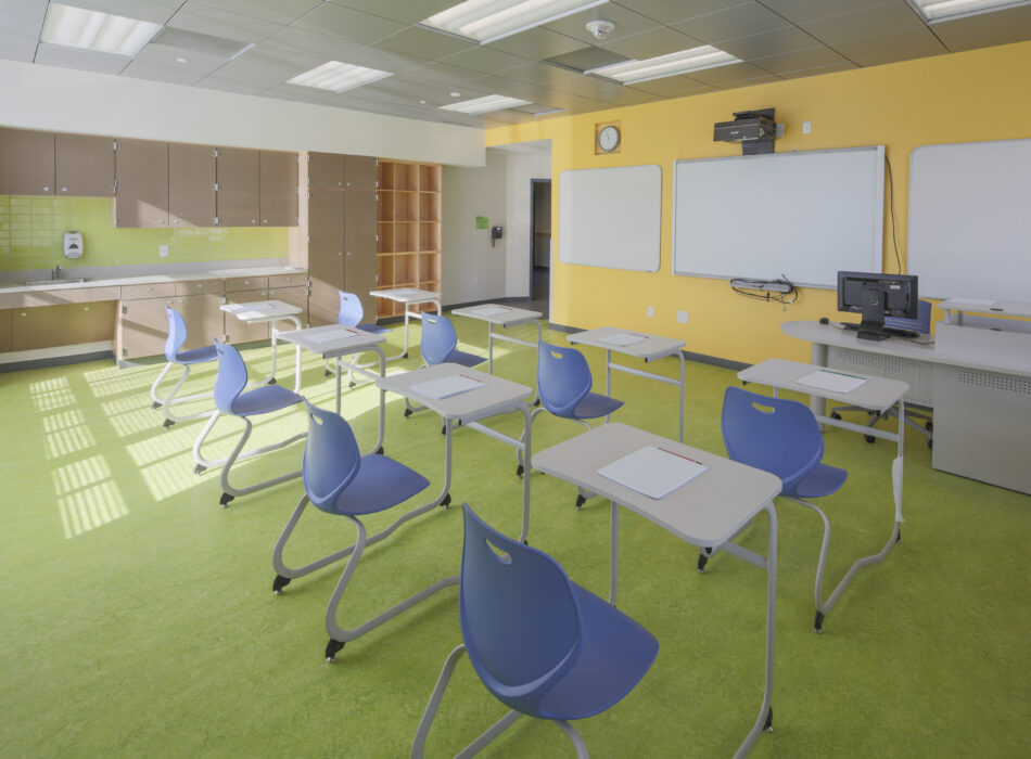 Modern classroom with yellow walls, blue chairs, white desks.