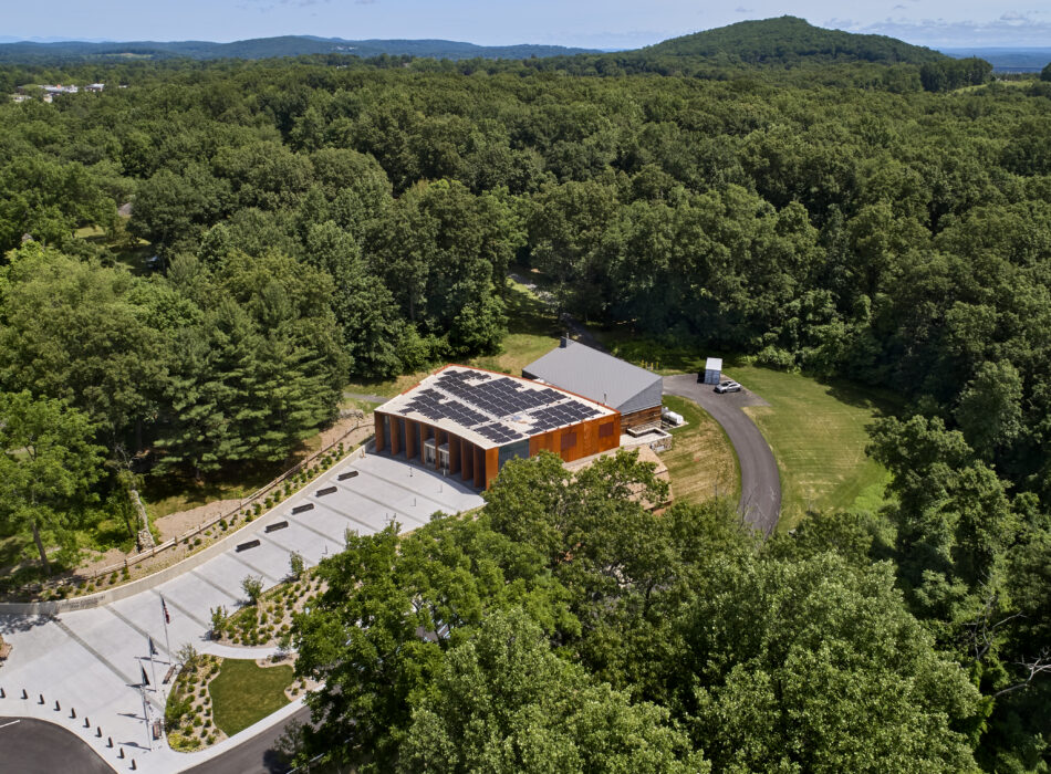 Modern building with rooftop solar panels amid trees and hills.