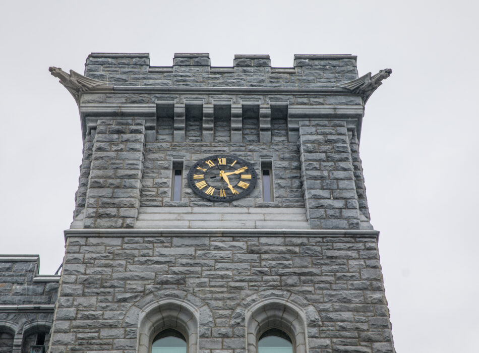 Stone clock tower with gold numerals, overcast sky.