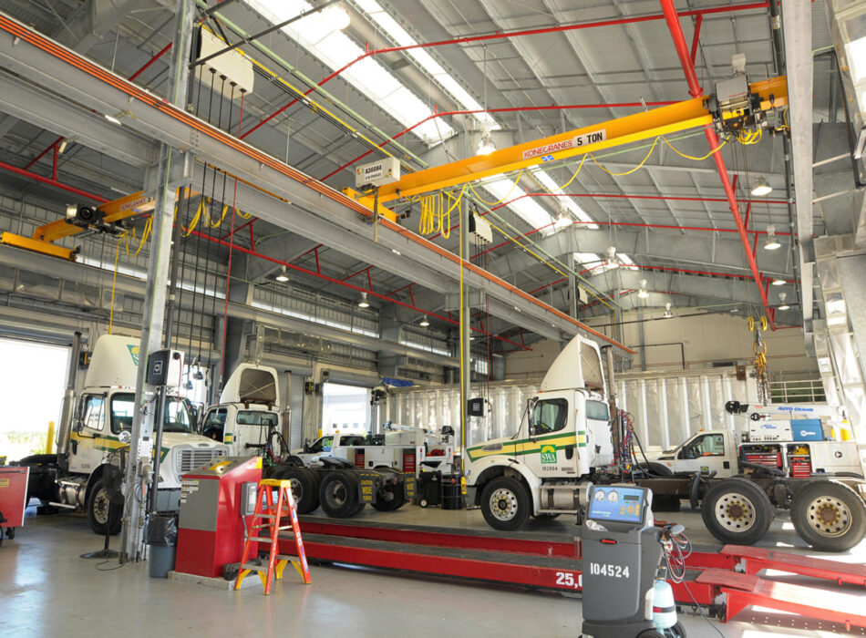 Truck garage interior with trucks, tools, and bright lighting.