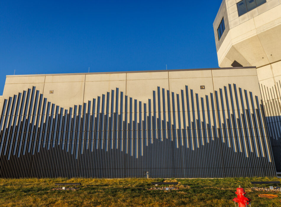 Wavy metal bars on beige building, red hydrant in front.