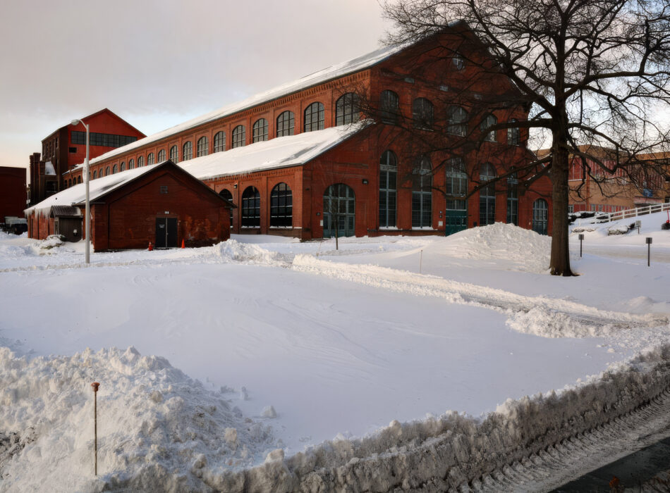 Red brick building by snowy yard and leafless tree.