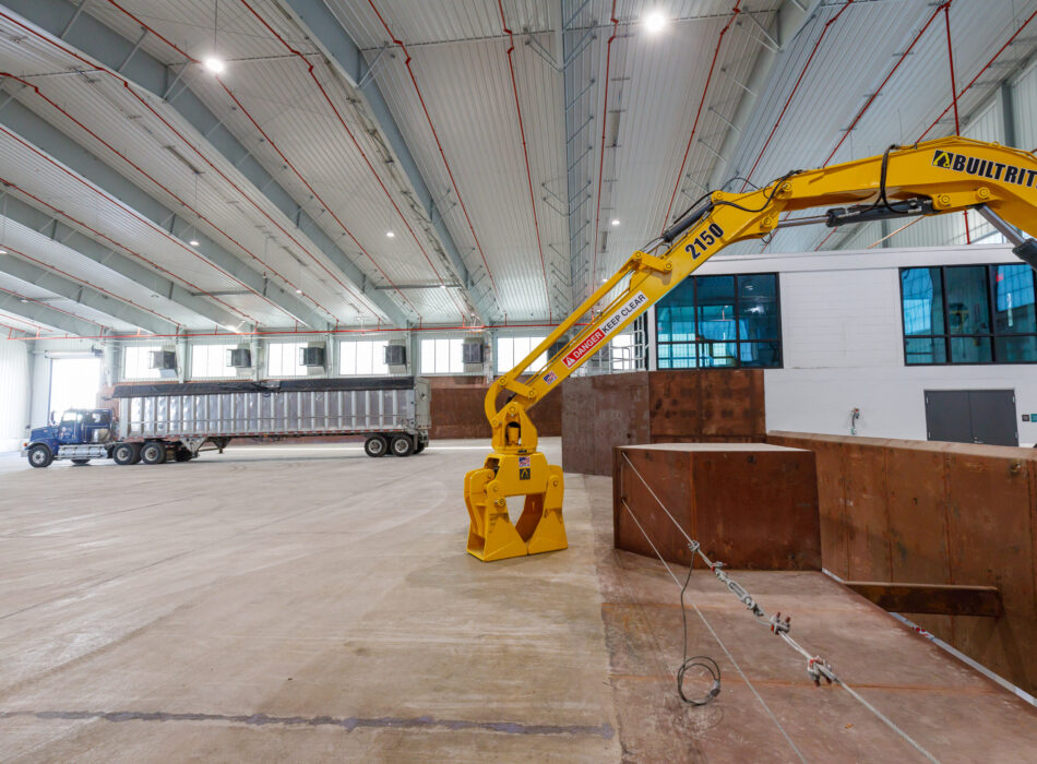Yellow excavator and trailer truck inside a large warehouse.