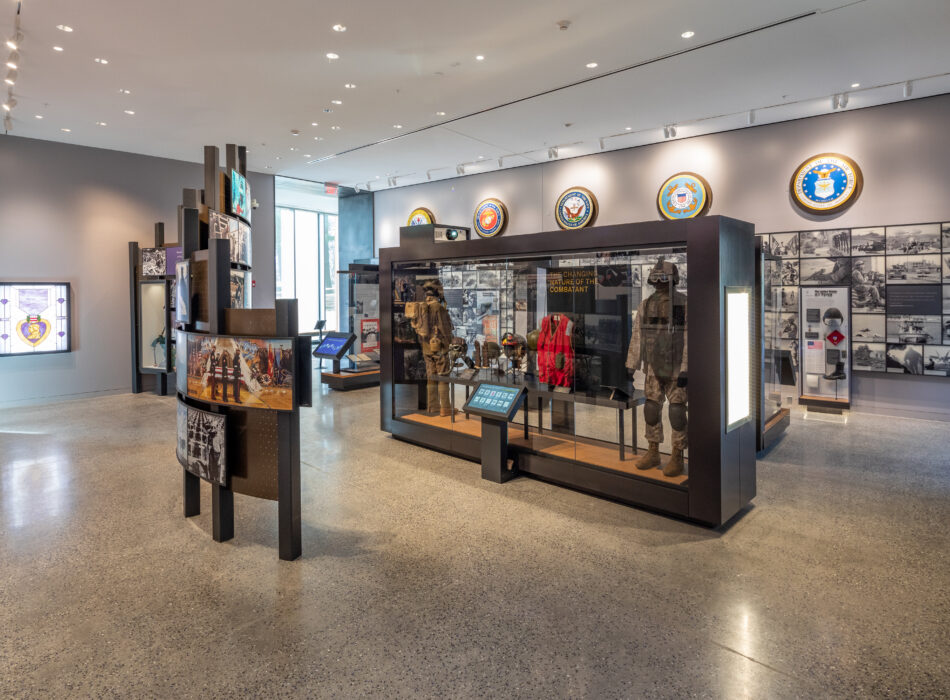 Museum exhibit with uniforms, equipment, panels, and emblems.